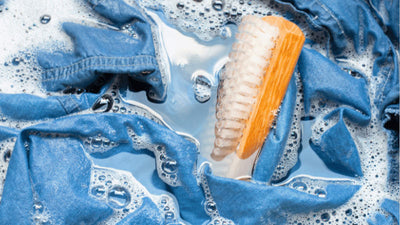 A person washing a pair of raw denim jeans by hand